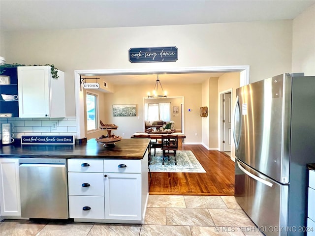 kitchen featuring appliances with stainless steel finishes, backsplash, a notable chandelier, white cabinetry, and hanging light fixtures