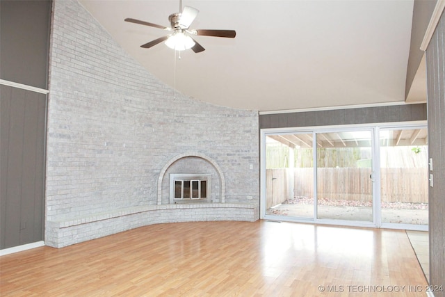 unfurnished living room featuring ceiling fan, wood walls, wood-type flooring, and a brick fireplace