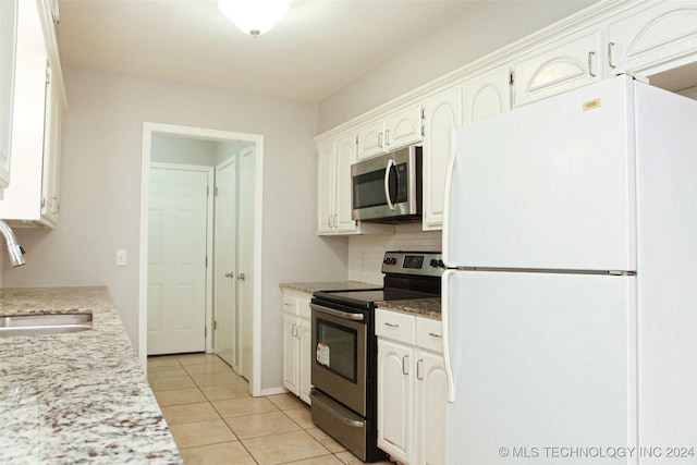 kitchen with sink, light tile patterned floors, appliances with stainless steel finishes, light stone counters, and white cabinetry