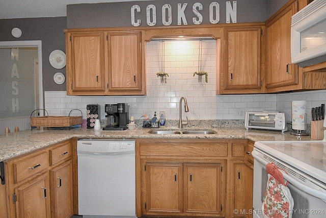 kitchen with decorative backsplash, light stone countertops, white appliances, and sink