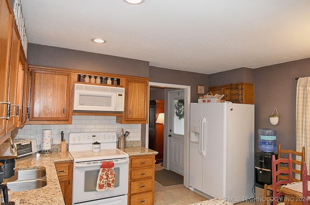 kitchen with decorative backsplash, light stone countertops, white appliances, and sink