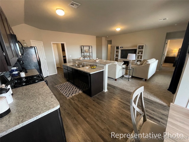 kitchen featuring light stone countertops, sink, black appliances, lofted ceiling, and an island with sink