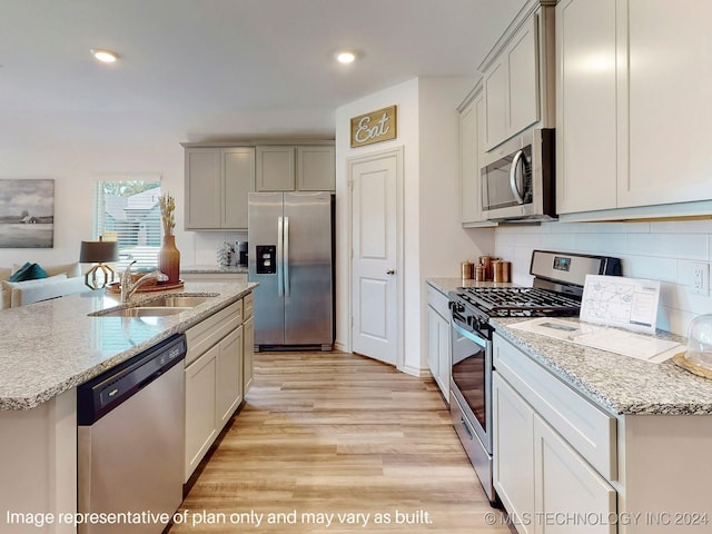 kitchen featuring a kitchen island with sink, sink, appliances with stainless steel finishes, tasteful backsplash, and light hardwood / wood-style floors