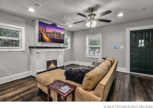 living room with hardwood / wood-style floors, ceiling fan, a stone fireplace, and a textured ceiling