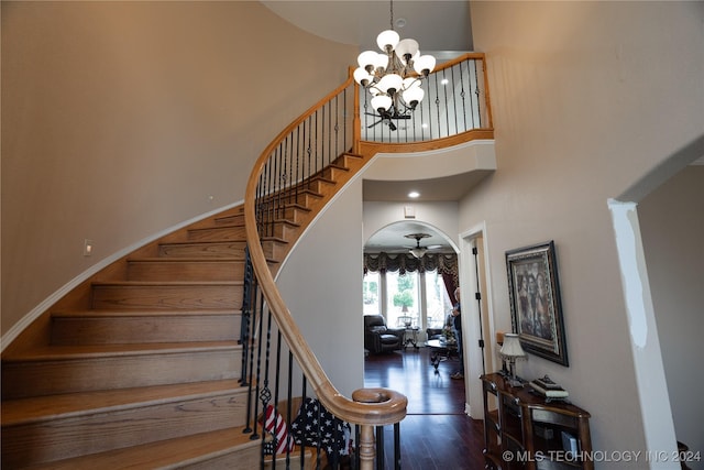 stairs with a high ceiling, ceiling fan with notable chandelier, and wood-type flooring