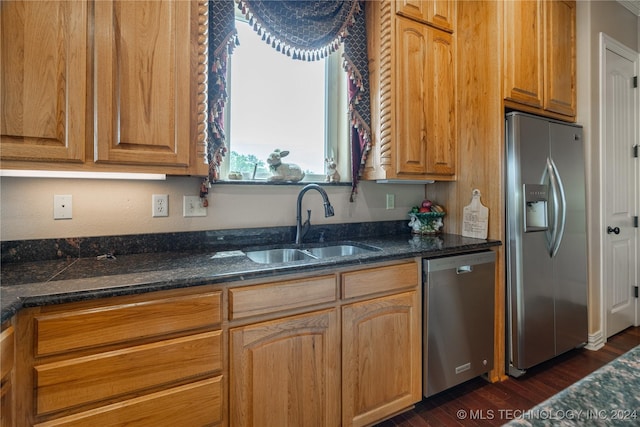 kitchen featuring appliances with stainless steel finishes, dark hardwood / wood-style floors, dark stone countertops, and sink