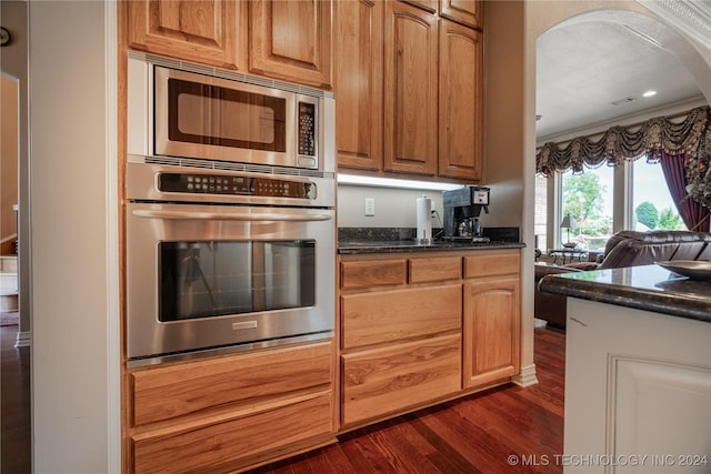 kitchen featuring appliances with stainless steel finishes, dark hardwood / wood-style flooring, crown molding, and dark stone countertops