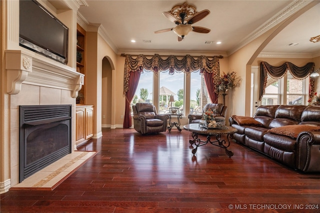 living room with dark hardwood / wood-style floors, ceiling fan, crown molding, and a tiled fireplace