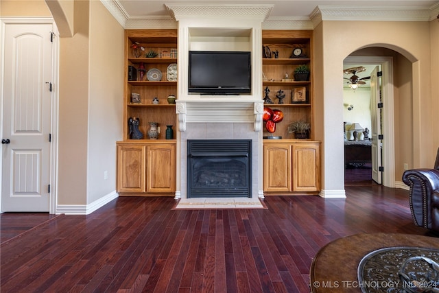 living room featuring dark hardwood / wood-style flooring, built in shelves, ceiling fan, crown molding, and a fireplace