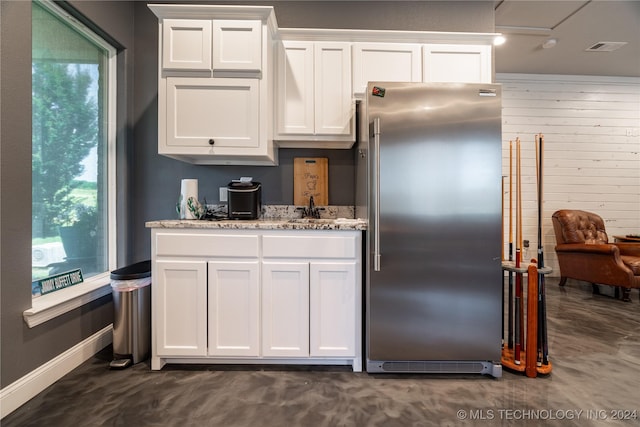 kitchen featuring light stone counters, high quality fridge, sink, white cabinetry, and wood walls