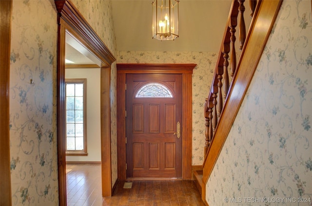 foyer entrance featuring ornamental molding, dark wood-type flooring, and a notable chandelier