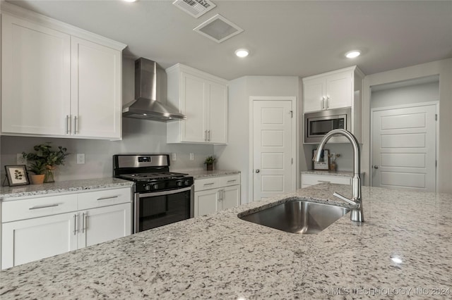 kitchen with light stone counters, sink, stainless steel appliances, and wall chimney range hood