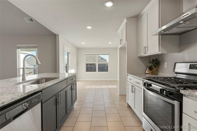 kitchen featuring light stone countertops, appliances with stainless steel finishes, wall chimney exhaust hood, sink, and white cabinets