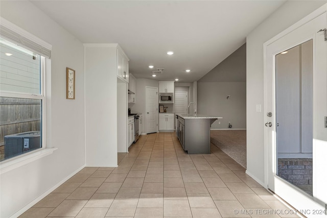 kitchen with light tile patterned floors, a kitchen bar, a kitchen island with sink, white cabinets, and appliances with stainless steel finishes