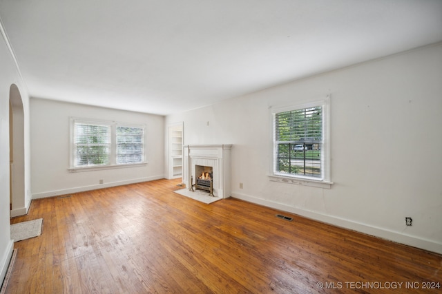 unfurnished living room with built in features, wood-type flooring, and a wealth of natural light