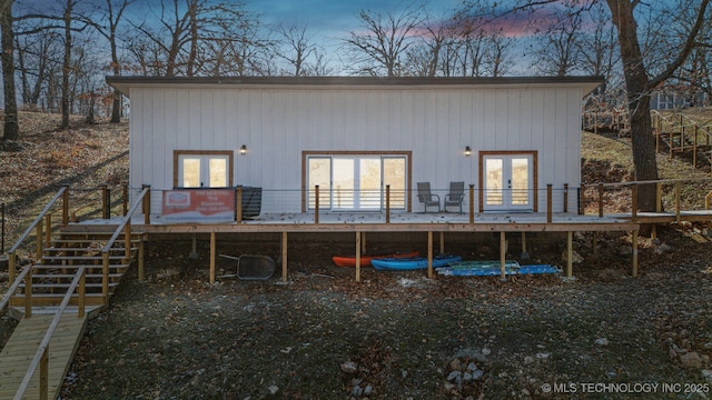 back house at dusk with a wooden deck and french doors