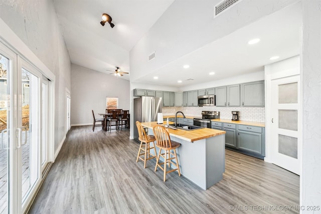 kitchen with tasteful backsplash, stainless steel appliances, ceiling fan, sink, and butcher block countertops