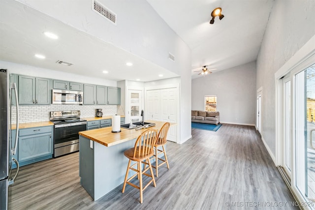 kitchen featuring butcher block counters, stainless steel appliances, vaulted ceiling, a breakfast bar area, and decorative backsplash