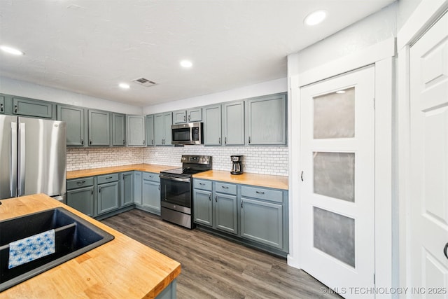 kitchen featuring dark hardwood / wood-style flooring, stainless steel appliances, tasteful backsplash, and butcher block counters