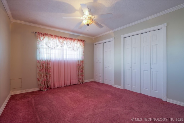 unfurnished bedroom with carpet, ceiling fan, crown molding, and two closets