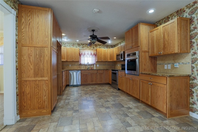 kitchen with ceiling fan, sink, stainless steel appliances, light stone counters, and a textured ceiling