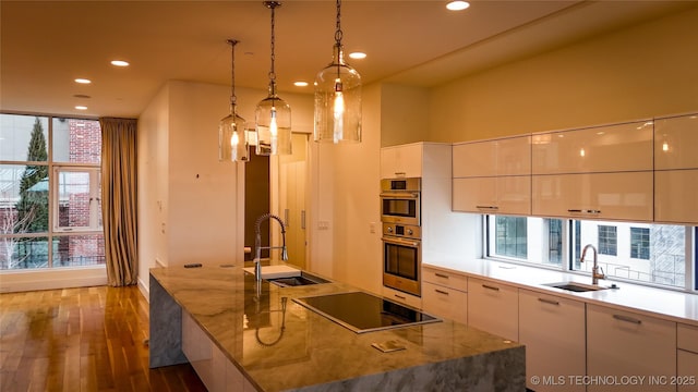 kitchen featuring a large island with sink, sink, hanging light fixtures, and black electric stovetop