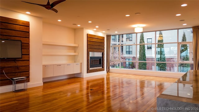 living room with light wood-type flooring, expansive windows, built in shelves, ceiling fan, and a fireplace