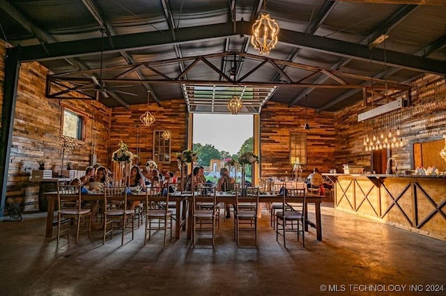 unfurnished dining area featuring wooden walls, high vaulted ceiling, and concrete floors