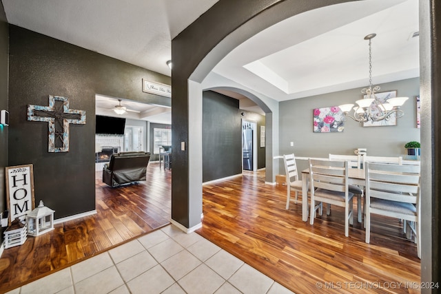 tiled dining space featuring ceiling fan with notable chandelier and a tray ceiling