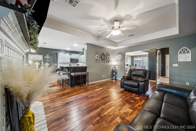 living room with a tray ceiling, hardwood / wood-style floors, ceiling fan with notable chandelier, and ornamental molding