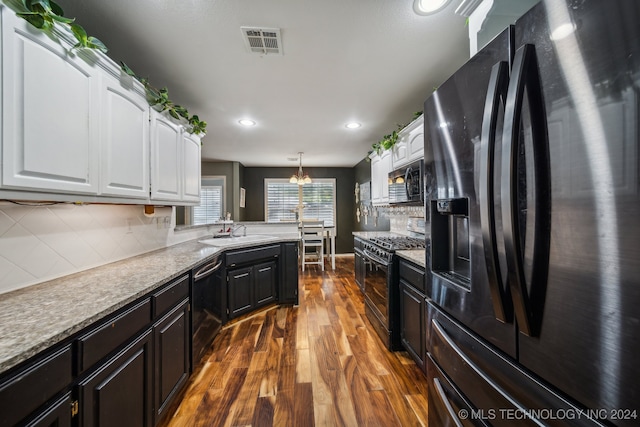 kitchen featuring backsplash, black appliances, an inviting chandelier, white cabinets, and hanging light fixtures