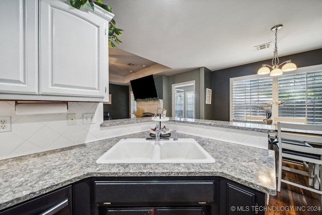 kitchen with backsplash, sink, light stone counters, white cabinetry, and a chandelier