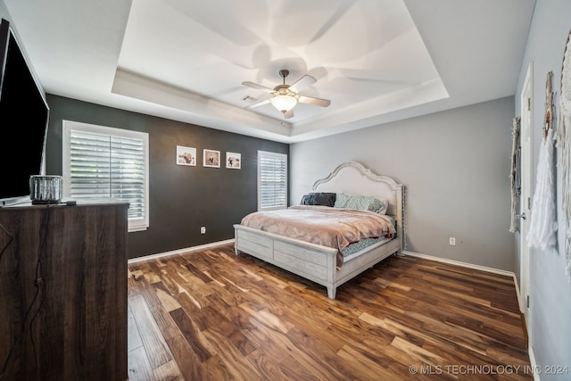 bedroom with ceiling fan, dark hardwood / wood-style flooring, and a tray ceiling