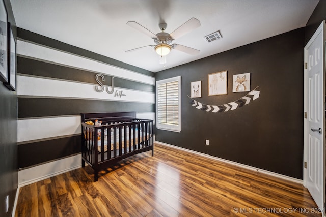 bedroom featuring ceiling fan, hardwood / wood-style floors, and a crib