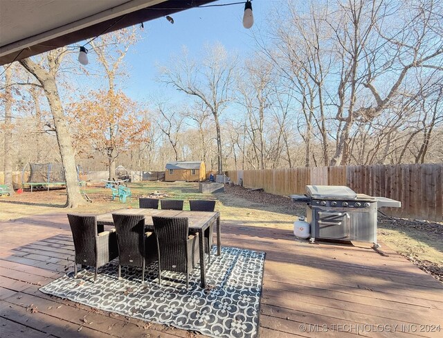 wooden deck featuring a shed, a trampoline, and grilling area