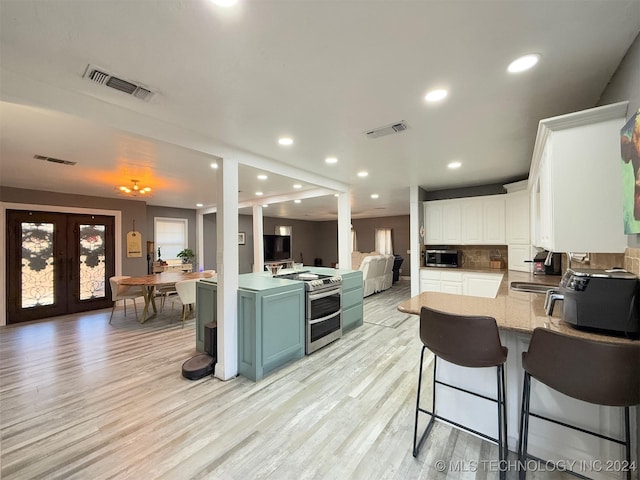 kitchen with appliances with stainless steel finishes, french doors, tasteful backsplash, light hardwood / wood-style floors, and white cabinetry