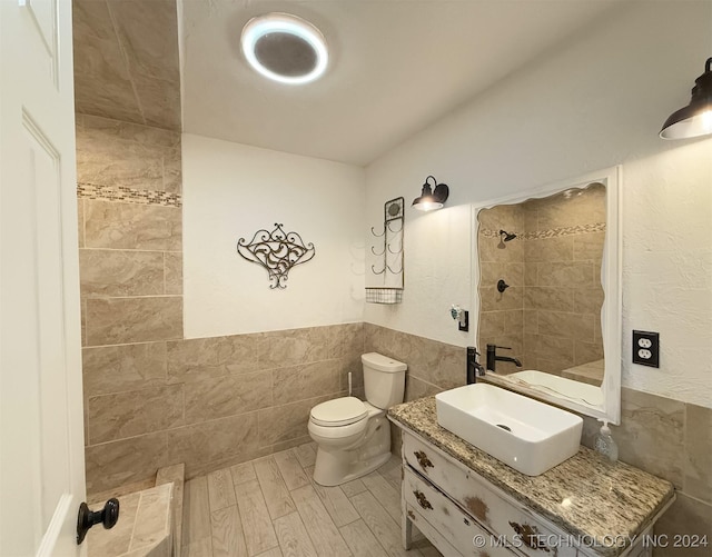 bathroom with vanity, toilet, tiled shower, and tile walls