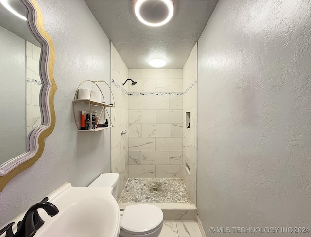 bathroom featuring tiled shower, a textured ceiling, toilet, and sink