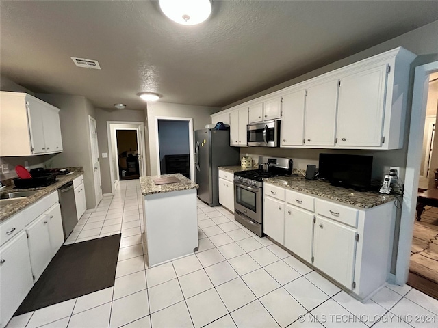 kitchen with appliances with stainless steel finishes, a textured ceiling, white cabinets, a kitchen island, and light tile patterned flooring