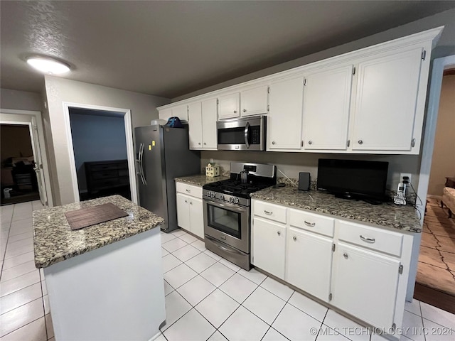 kitchen featuring white cabinetry, a center island, stainless steel appliances, dark stone counters, and light tile patterned floors