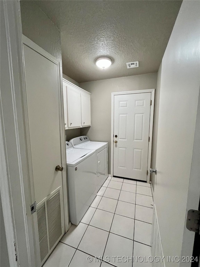 clothes washing area featuring cabinets, light tile patterned floors, a textured ceiling, and washing machine and clothes dryer