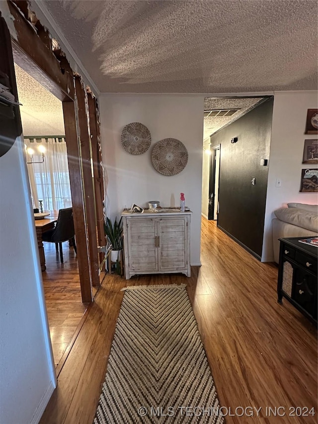 corridor with ornamental molding, a textured ceiling, and hardwood / wood-style flooring