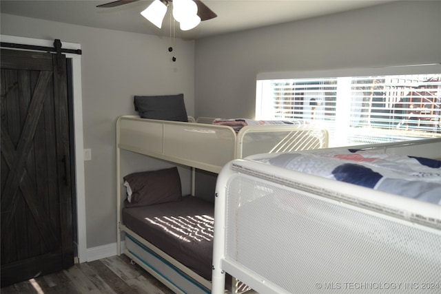 bedroom with a barn door, ceiling fan, and dark wood-type flooring