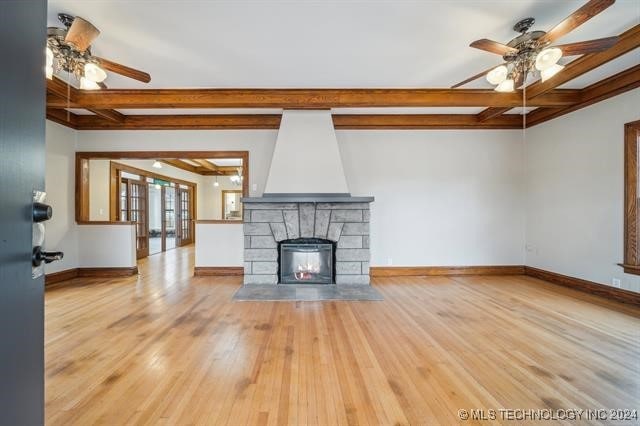 unfurnished living room featuring a fireplace, beam ceiling, light hardwood / wood-style flooring, and ceiling fan