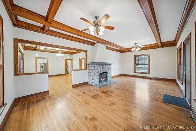 unfurnished living room with a stone fireplace, beamed ceiling, ceiling fan with notable chandelier, and light wood-type flooring