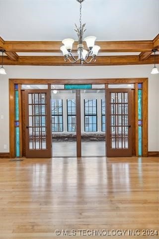 unfurnished dining area featuring beam ceiling, french doors, coffered ceiling, a notable chandelier, and wood-type flooring