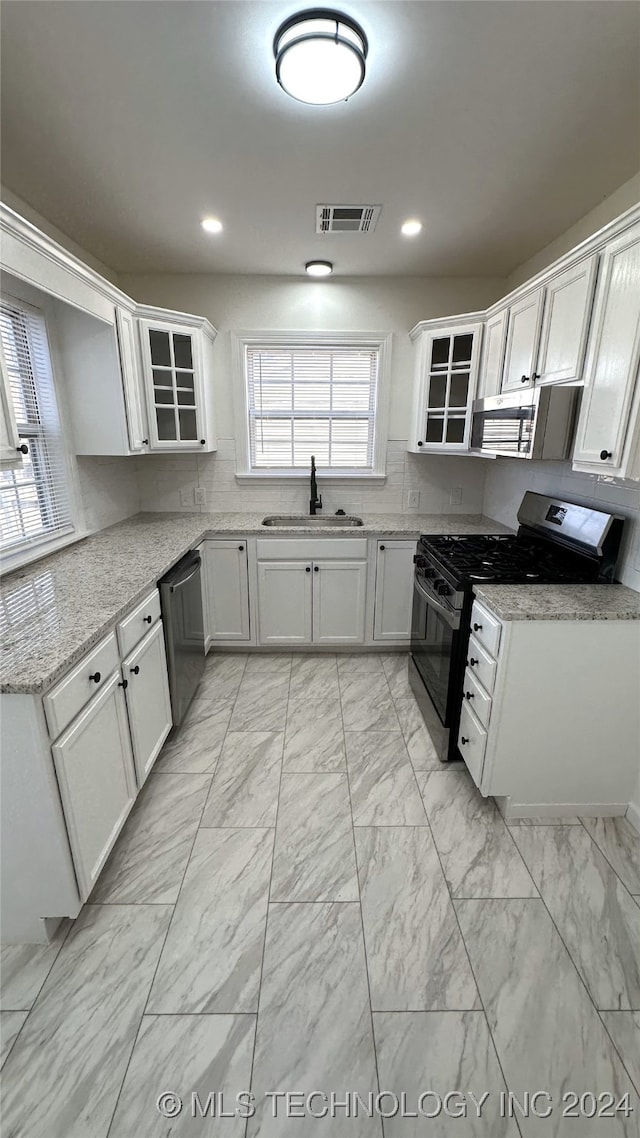 kitchen featuring tasteful backsplash, light stone counters, stainless steel appliances, sink, and white cabinets