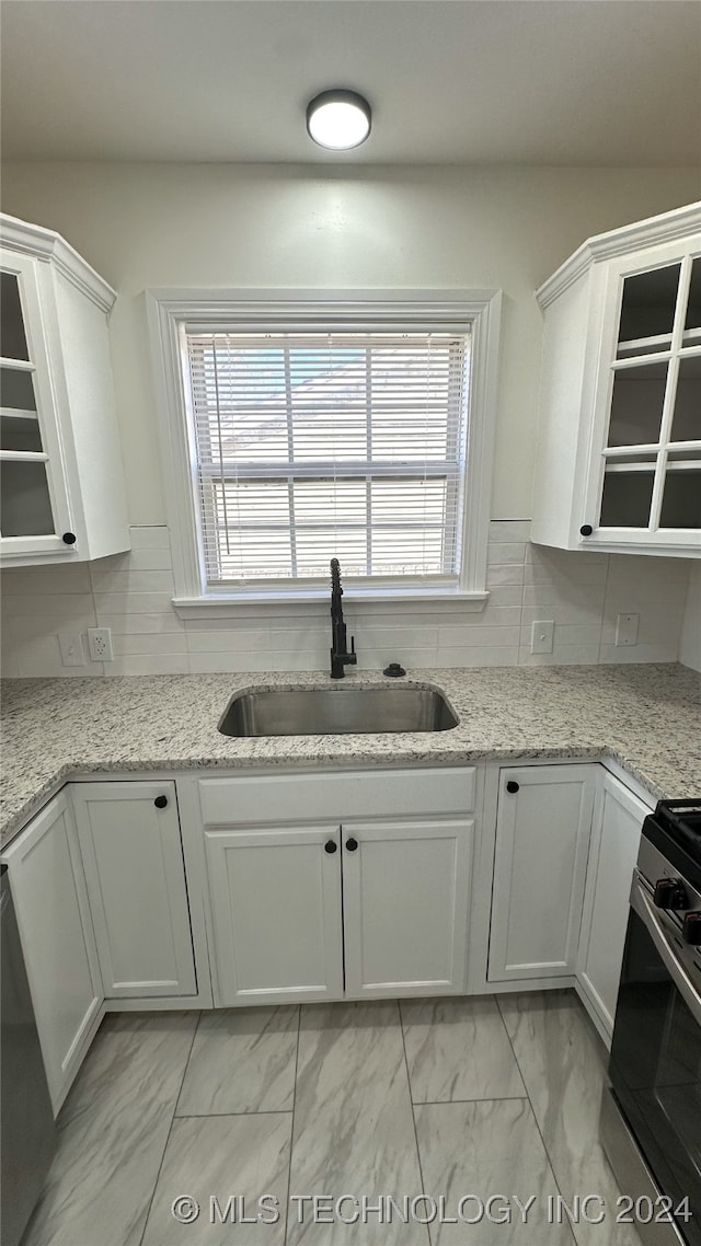 kitchen with white cabinets, light stone counters, sink, and stainless steel range