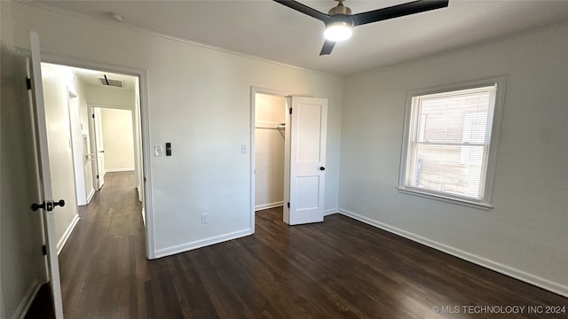 unfurnished bedroom with dark wood-type flooring, a walk in closet, crown molding, ceiling fan, and a closet