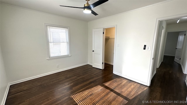 unfurnished bedroom with a walk in closet, ceiling fan, crown molding, dark wood-type flooring, and a closet